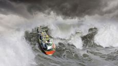 An oil tanker ship churns up a huge tsunami like wave in rough seas.