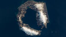 A satellite photo of a horseshoe-shape island partly covered in snow