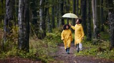 a couple wearing rain jackets with an umbrella walking in the rain in the forest