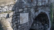 A photograph of an arched stone bridge with a plaque