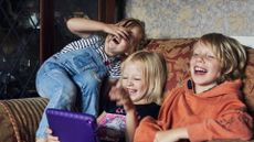 Three siblings sitting on a couch looking at an iPad and laughing