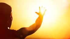 Young woman shown in silhouette as she's reaching for the sun.