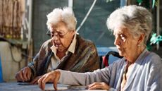 Two elderly women are sitting at a table. They appear to be playing cards.